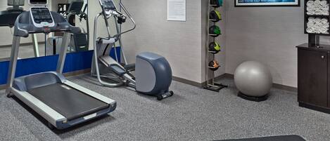 A fitness room with treadmills, elliptical machines, a stationary bike, a wall-mounted TV, a rack with exercise balls, and a mat.