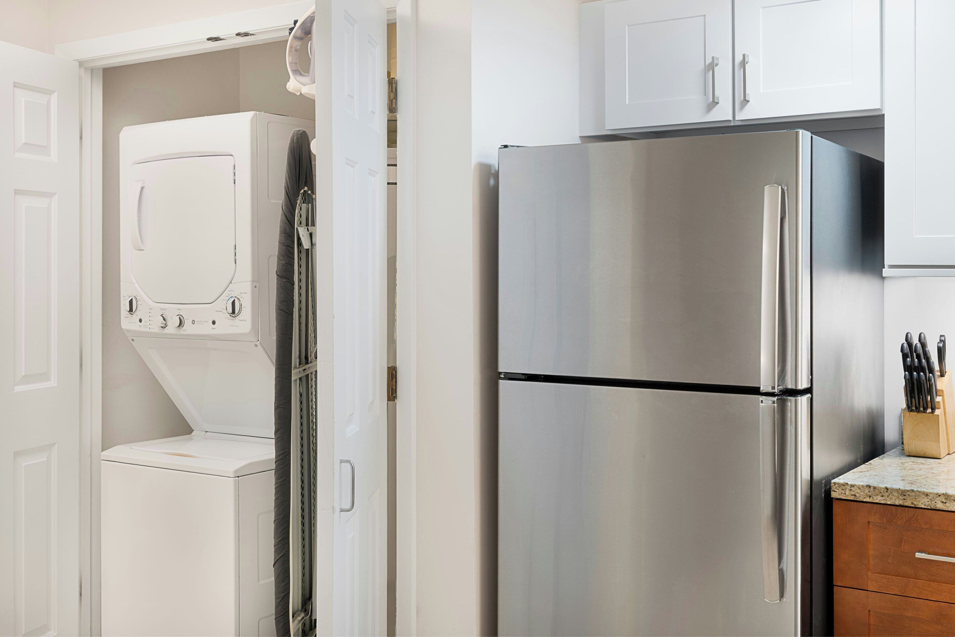 A compact kitchen with a stainless steel refrigerator, a built-in washer and dryer, and wooden cabinets.