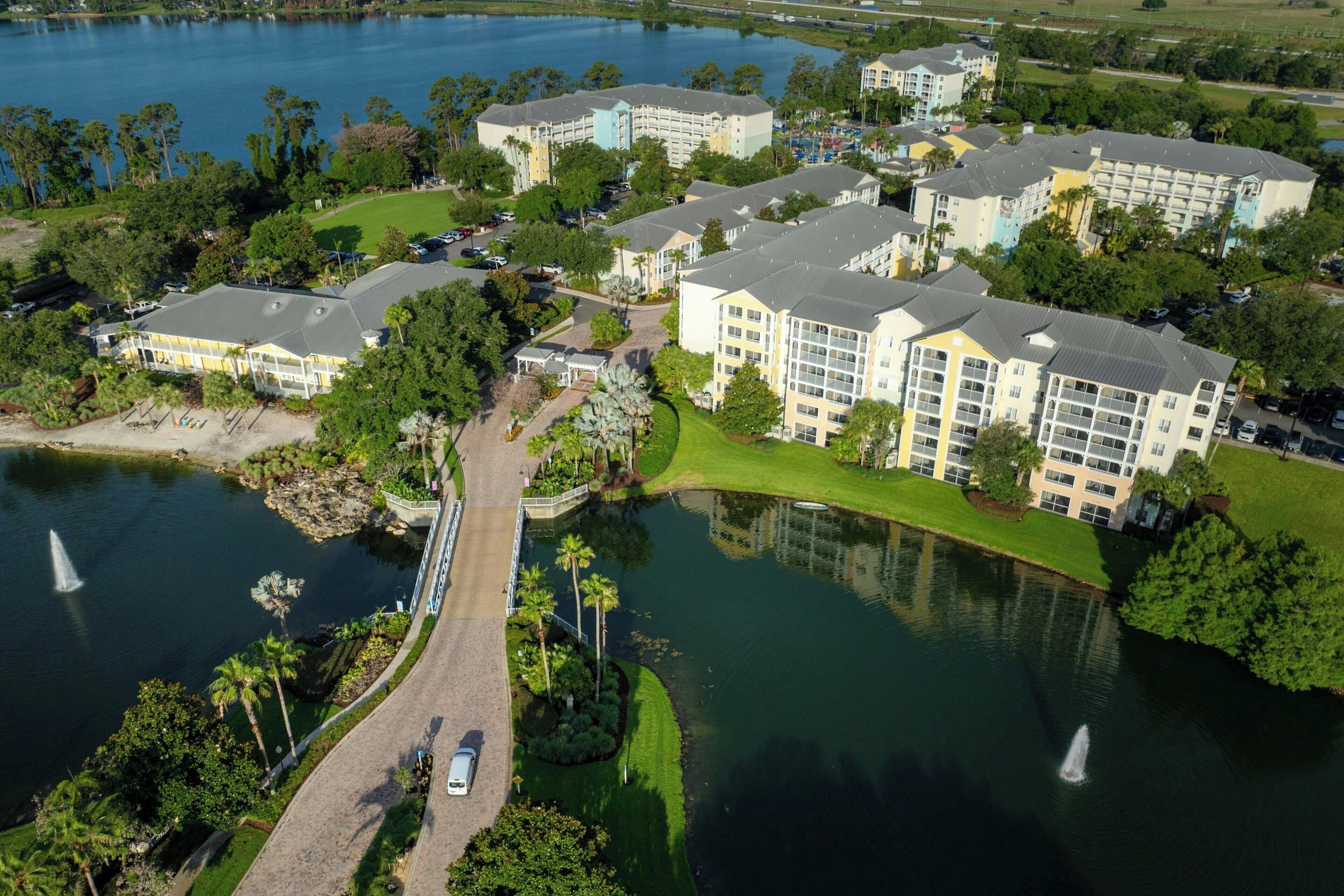 An aerial view of a hotel complex with multiple buildings, a bridge, and a lake.