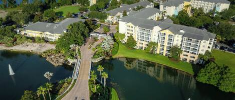 An aerial view of a hotel complex with multiple buildings, a bridge, and a lake.