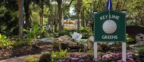 A sign for Key Lime Greens with a golf ball symbol, surrounded by lush greenery and flowering plants.