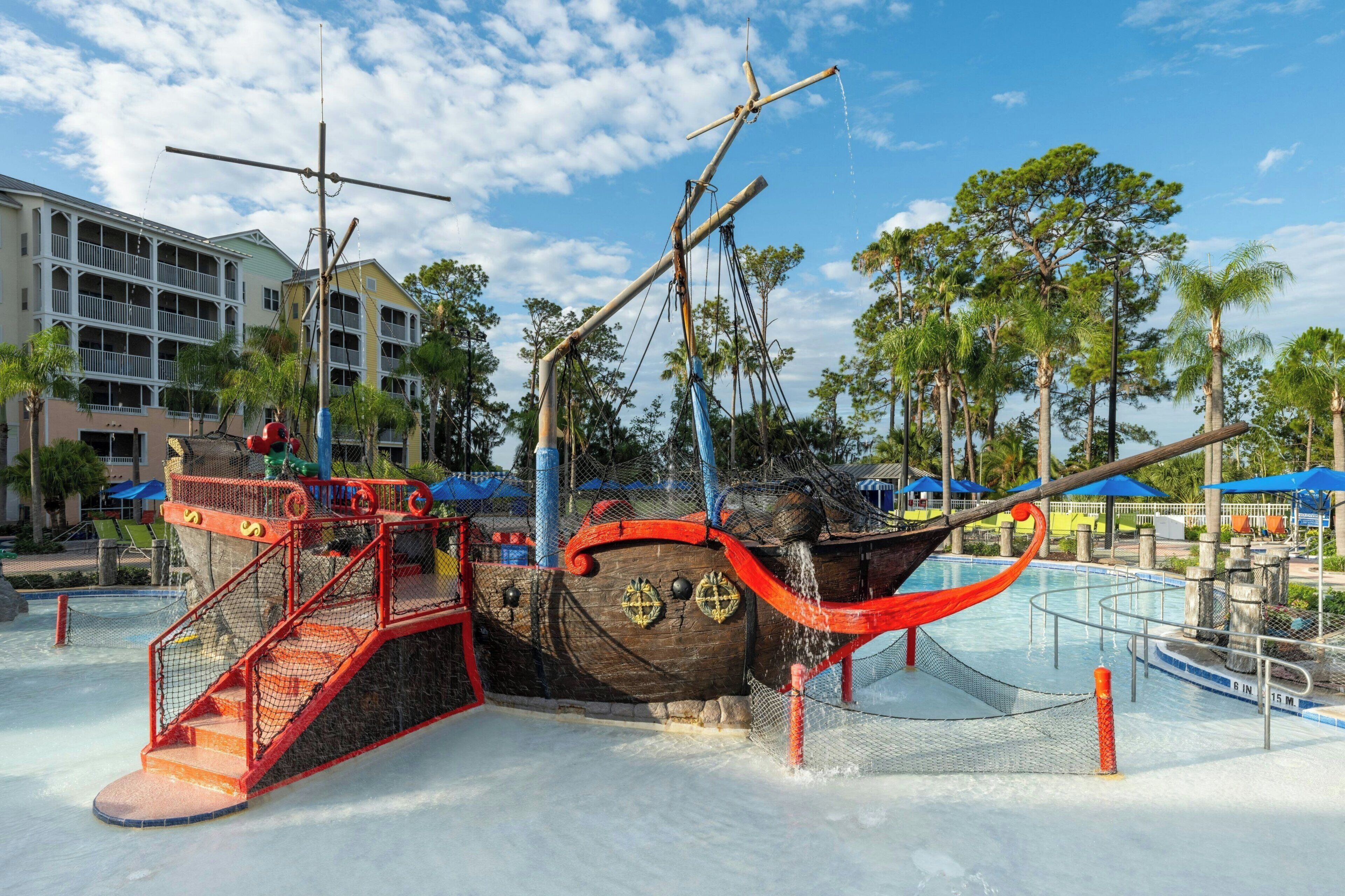 A water park with a pirate ship-themed water slide, a pool, and a building with balconies.