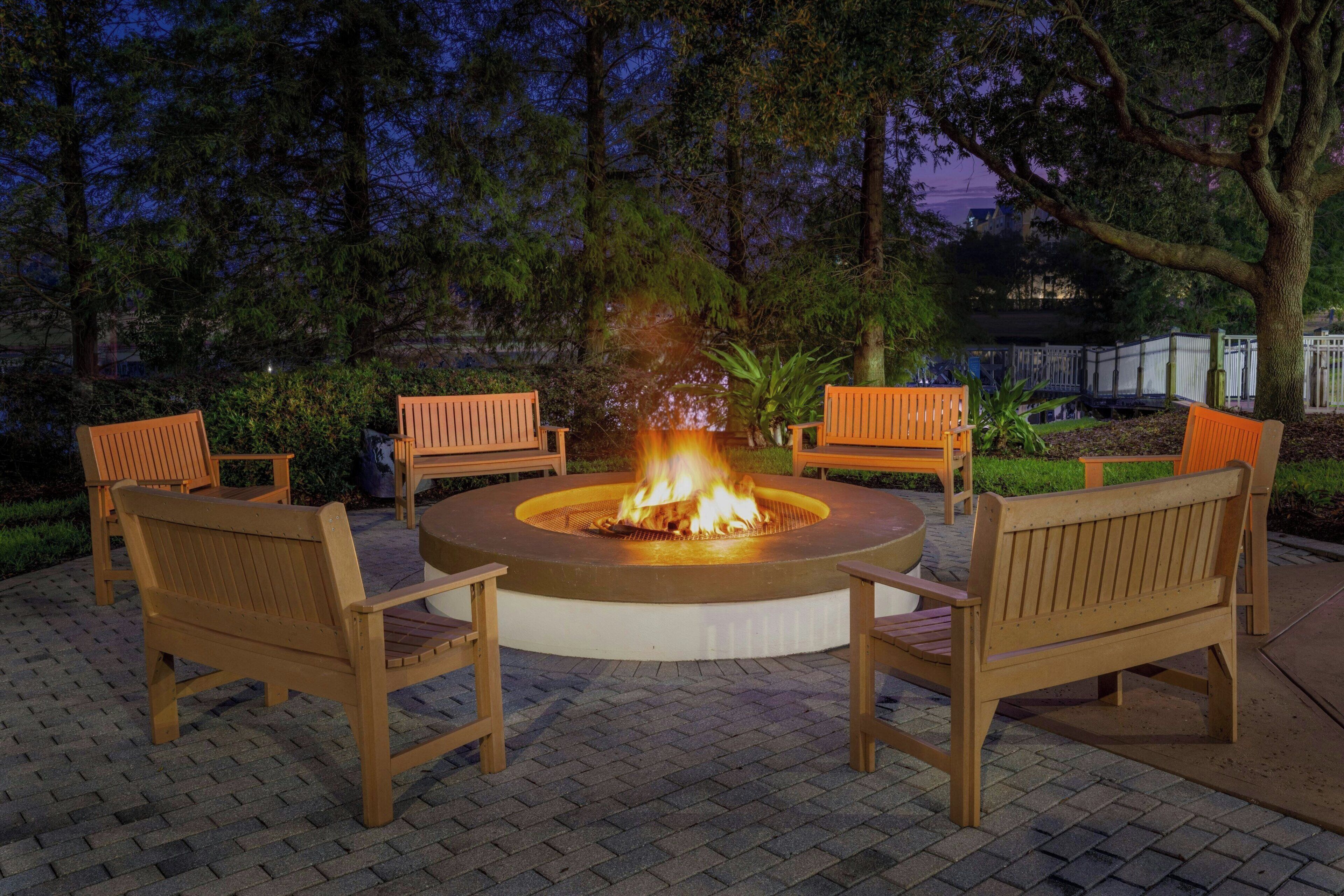 A circular outdoor seating area with a fire pit in the center, surrounded by wooden benches.