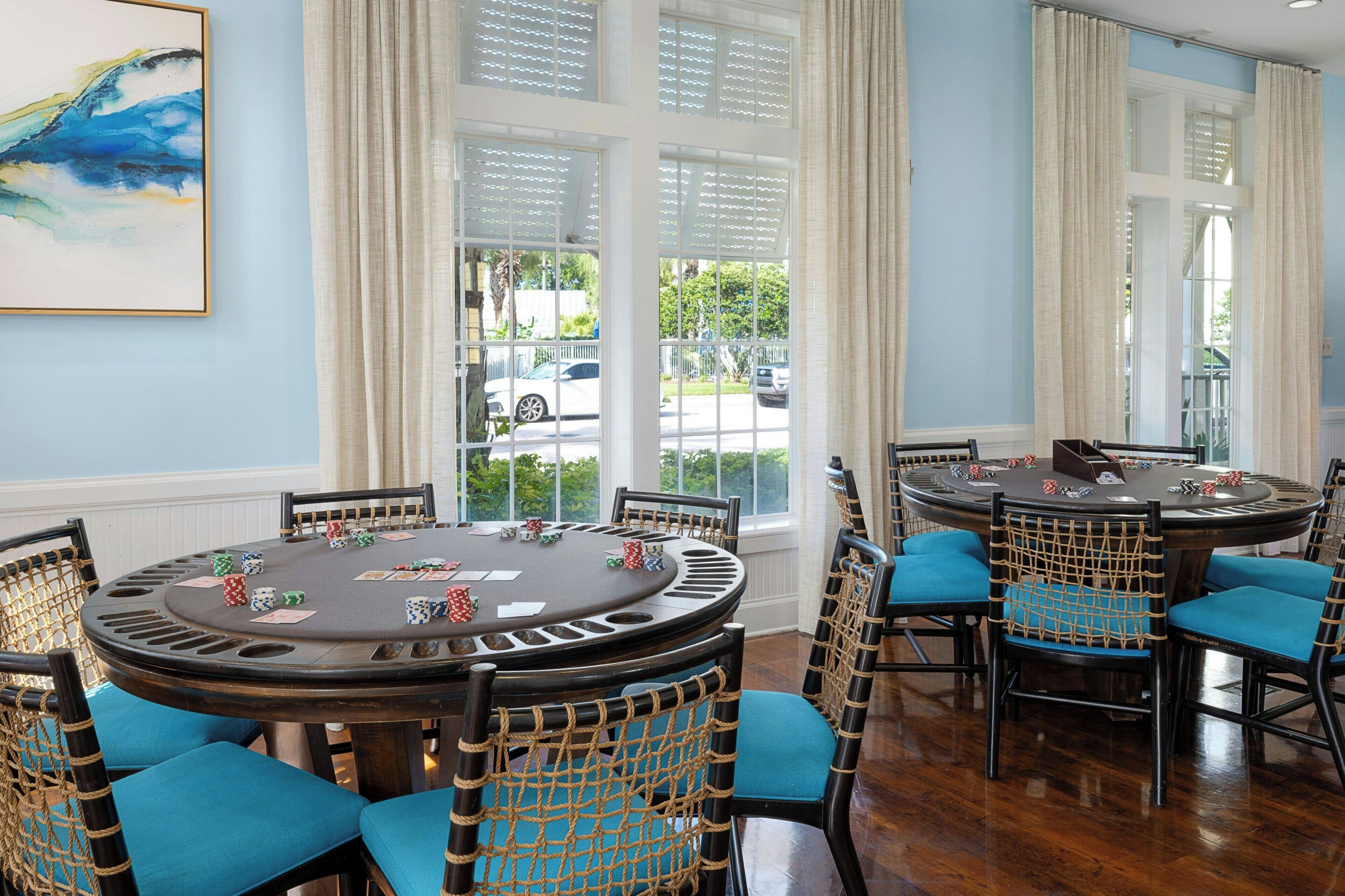 A room with multiple blackjack tables, chairs with rope netting, and large windows with curtains.