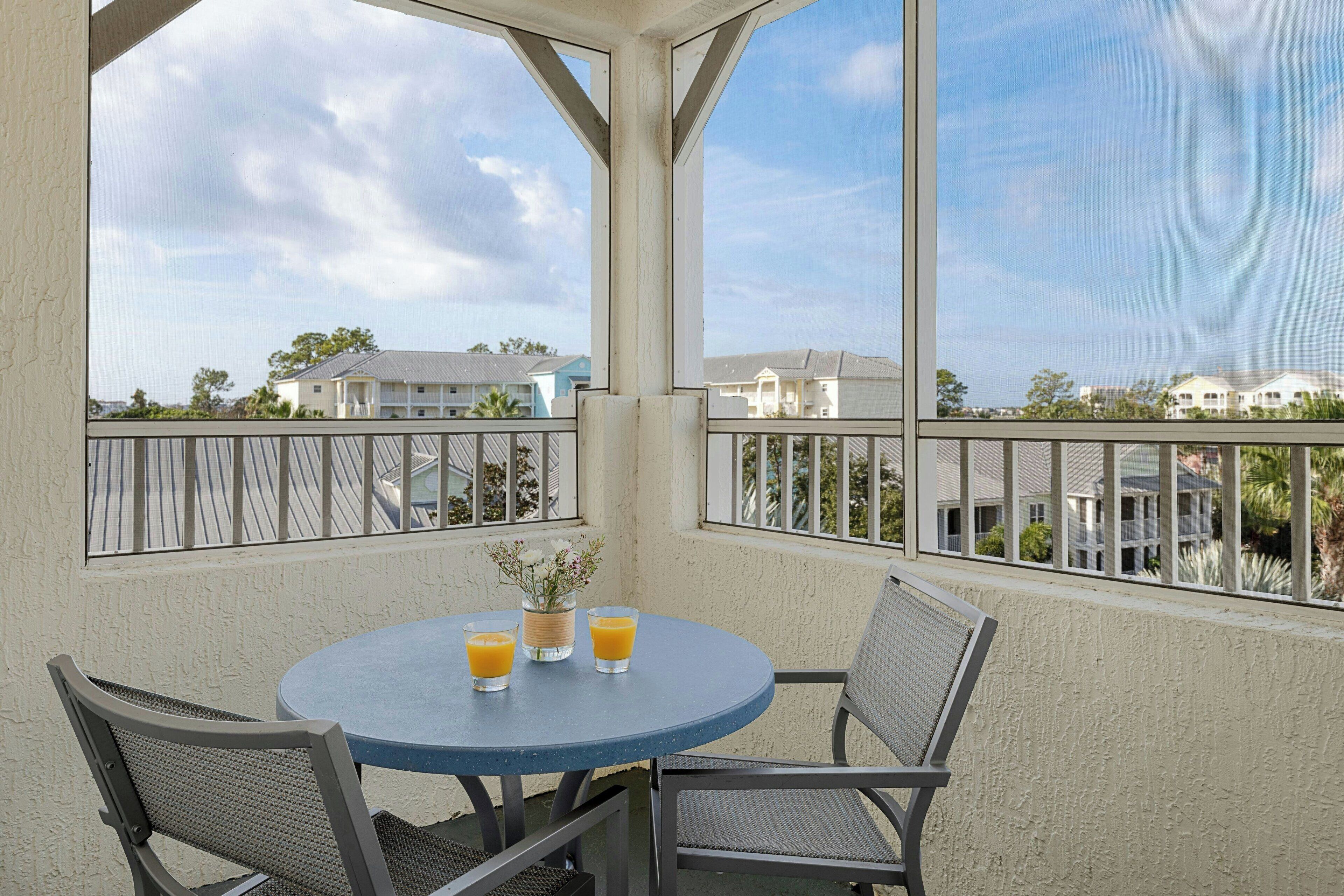 A balcony with a table set for two, two glasses of orange juice, and a vase with flowers.