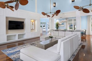 A spacious living room with a large flat-screen TV, white built-in shelving, a sectional sofa, and ceiling fans. - Marriott's Harbour Lake (Orlando)