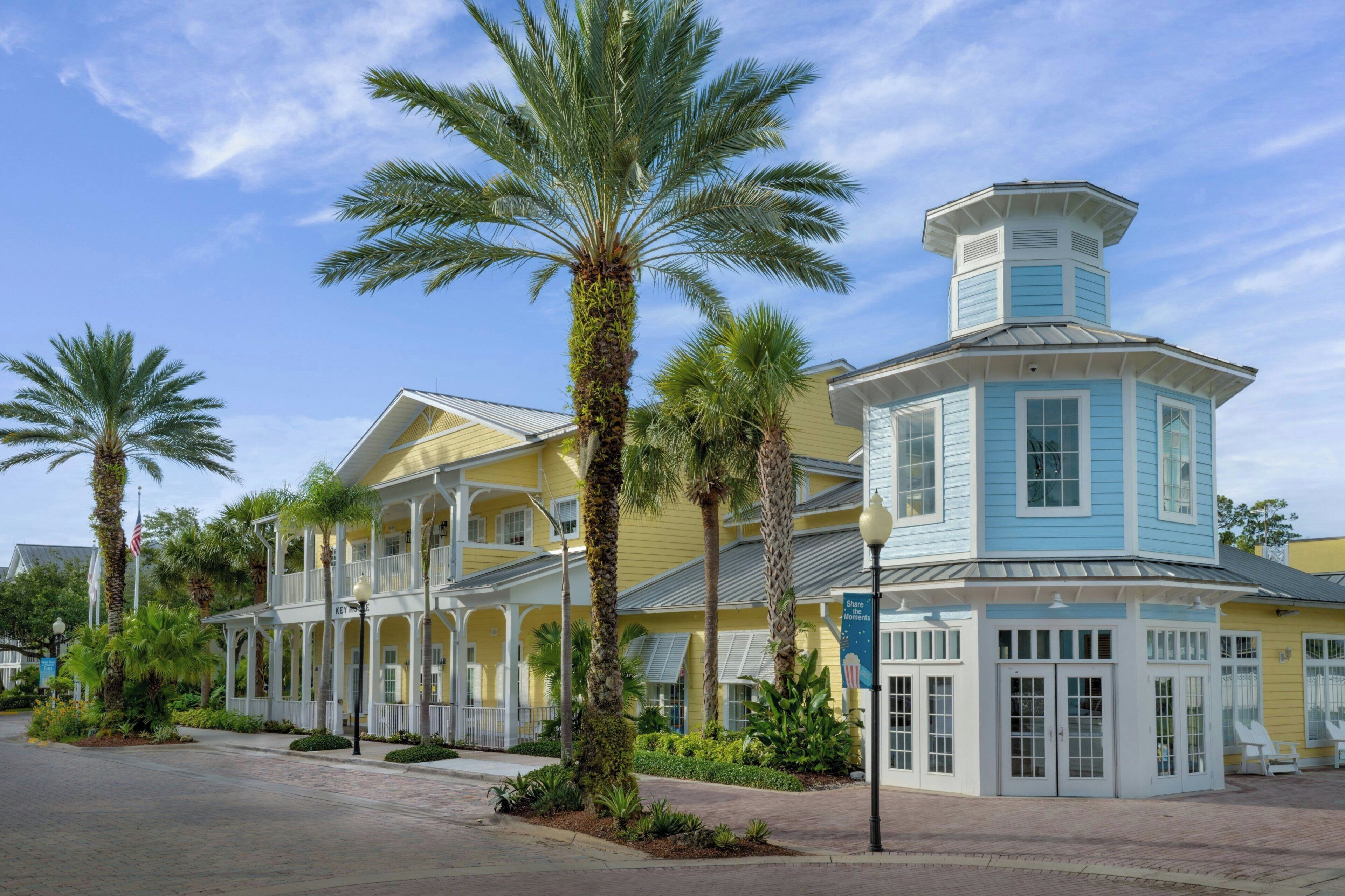 A yellow building with a blue tower, surrounded by palm trees.