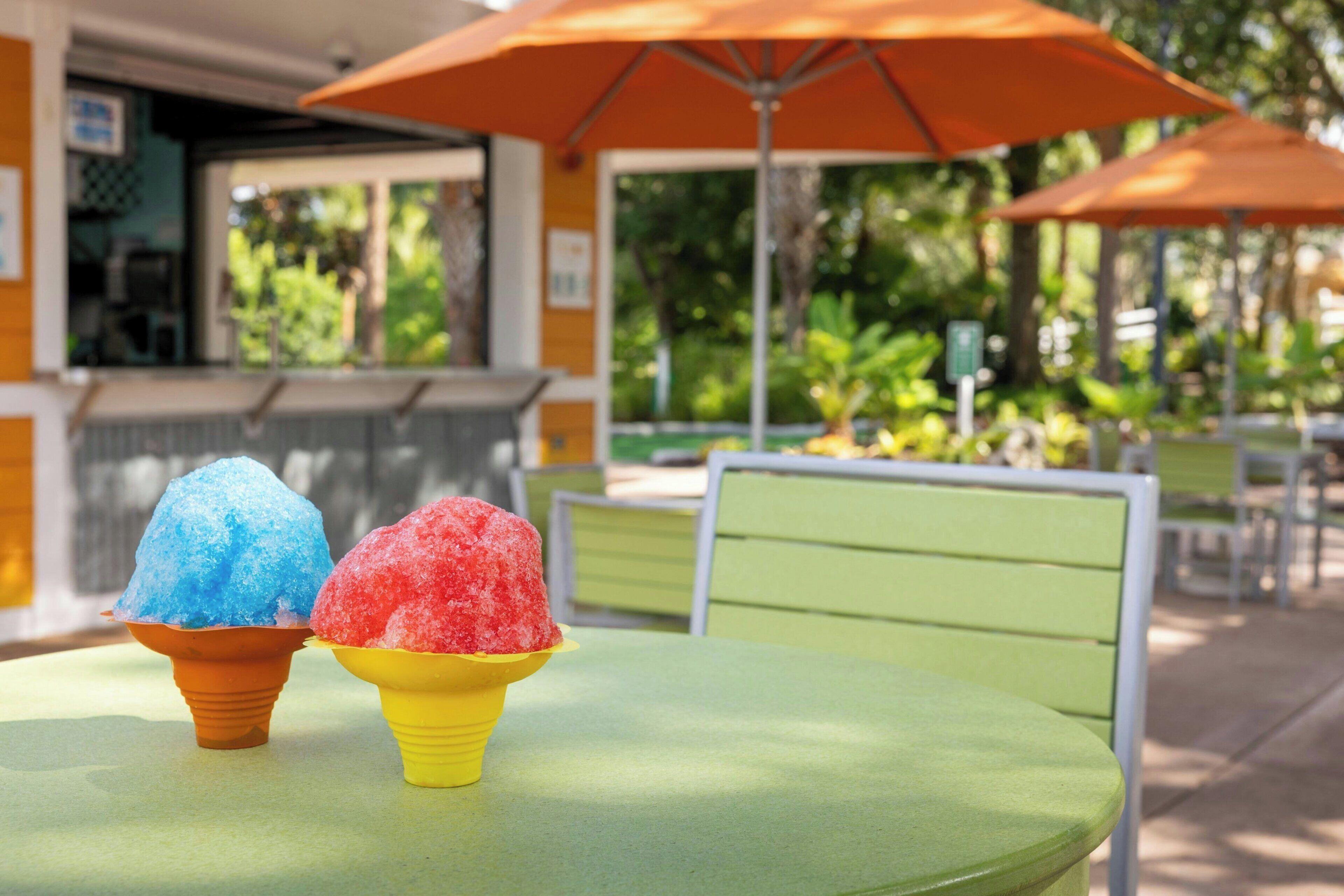 Une table avec deux cornets de glace, un bleu et un rouge, placés sous un parasol orange.
