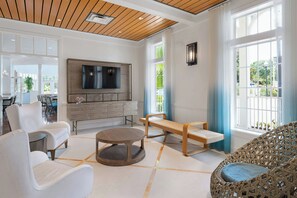 A modern living room with a flat-screen TV, white sofas, a wooden coffee table, and a wicker chair. - Marriott's Harbour Lake (Orlando)