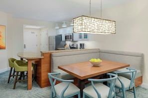 Una cocina moderna con una isla integrada, un comedor con mesa de madera y sillas azules, y una lámpara colgante.
