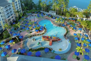 A resort with a large pool, multiple lounge areas with umbrellas, and a view of the ocean.