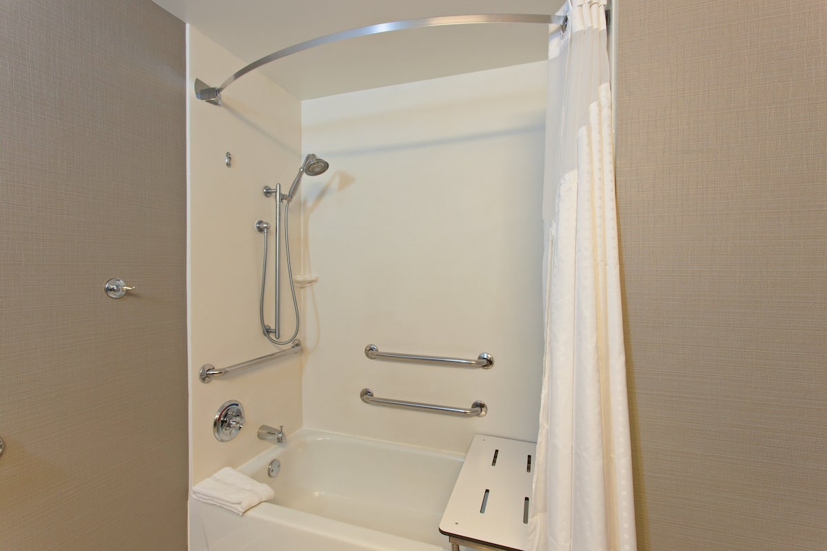 A bathroom with a bathtub, shower, grab bars, and a towel rack.