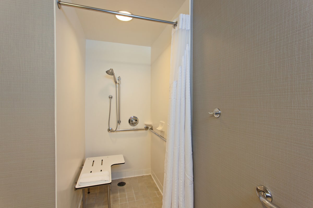 A small, modern bathroom with a shower, grab bar, and a sink with a towel.
