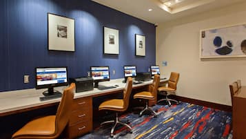 A conference room with four desks, each with a computer and a chair. There are framed pictures on the wall and a colorful carpet.