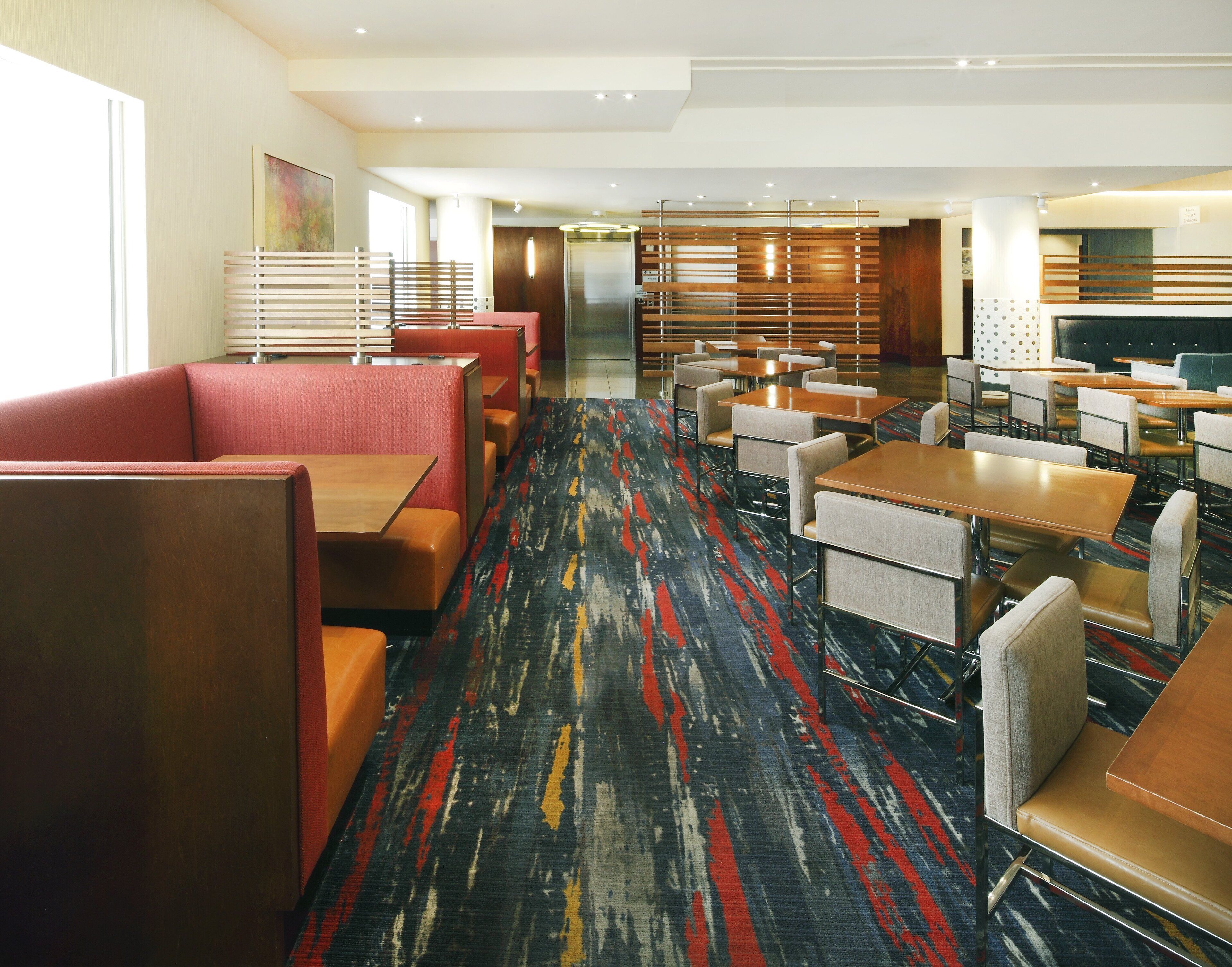 A hotel lobby with seating areas, a central elevator, and a patterned carpet.