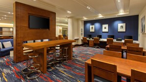 Un hall d’hôtel moderne avec un comptoir d’accueil en bois, des tabourets de bar et un coin salon doté de canapés bleus.