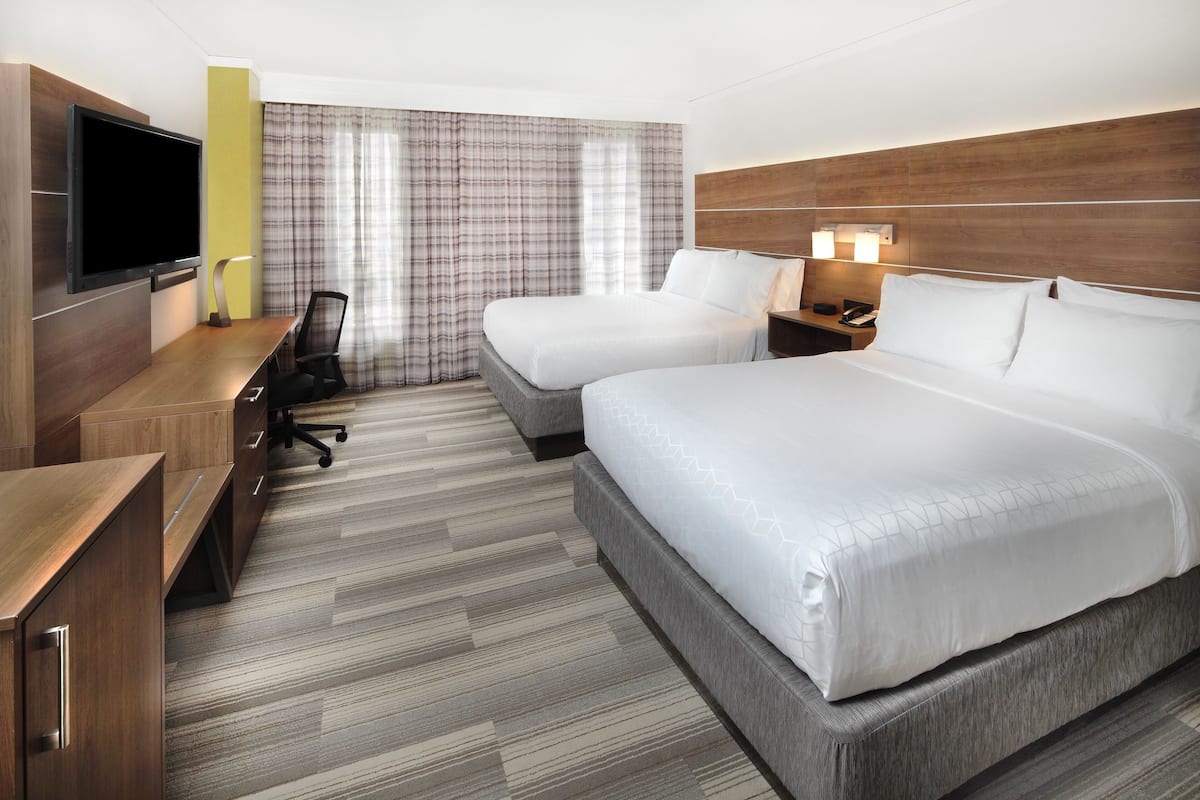 A hotel room with two beds, a desk, a TV, and a modern design.