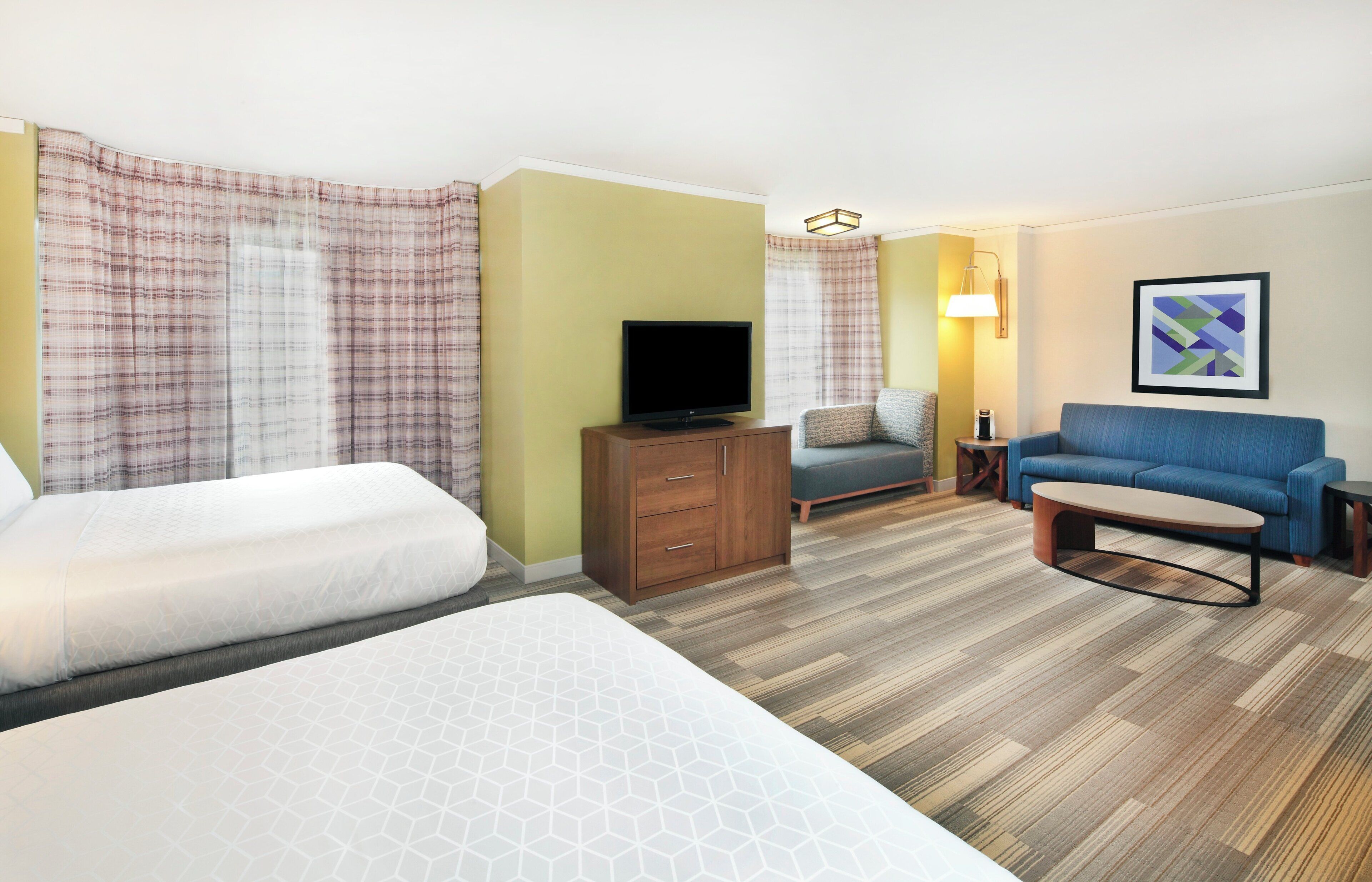 A hotel room with two beds, a television, a sofa, a small table, and a lamp.