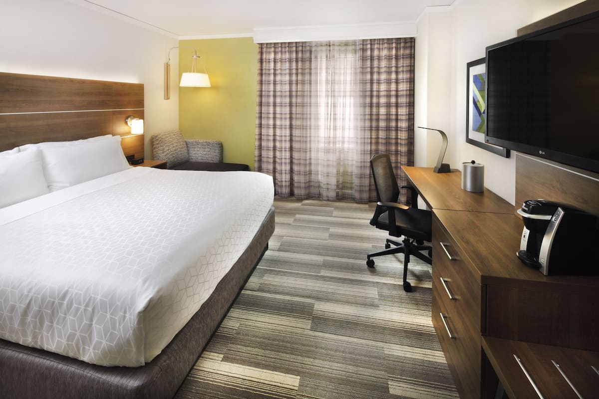 A hotel room with a large bed, a desk with a coffee maker, a TV, and a window with curtains.