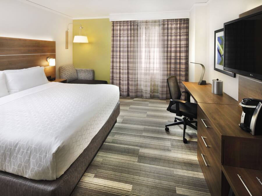 Habitación de hotel con una cama grande, un escritorio con cafetera, televisión y ventana con cortinas.