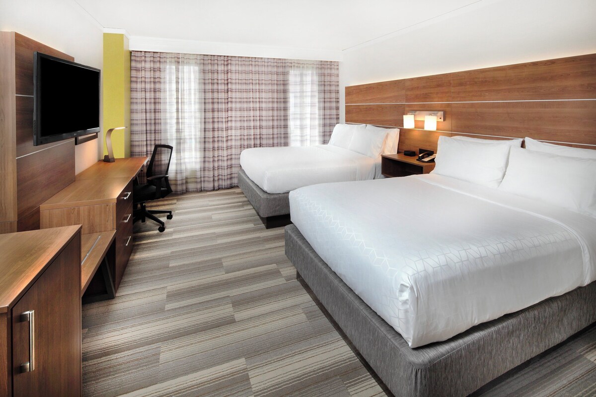 A hotel room with two beds, a desk with a chair, a TV, and a wooden headboard.