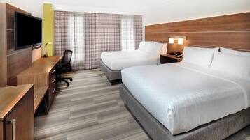 Habitación de hotel con dos camas, un escritorio con silla, un televisor y cabecera de madera.