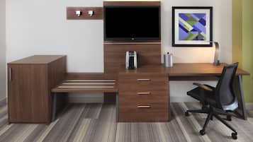 A modern office space with a wooden desk, a black office chair, a television, a coffee machine, and a framed abstract art piece on the wall.