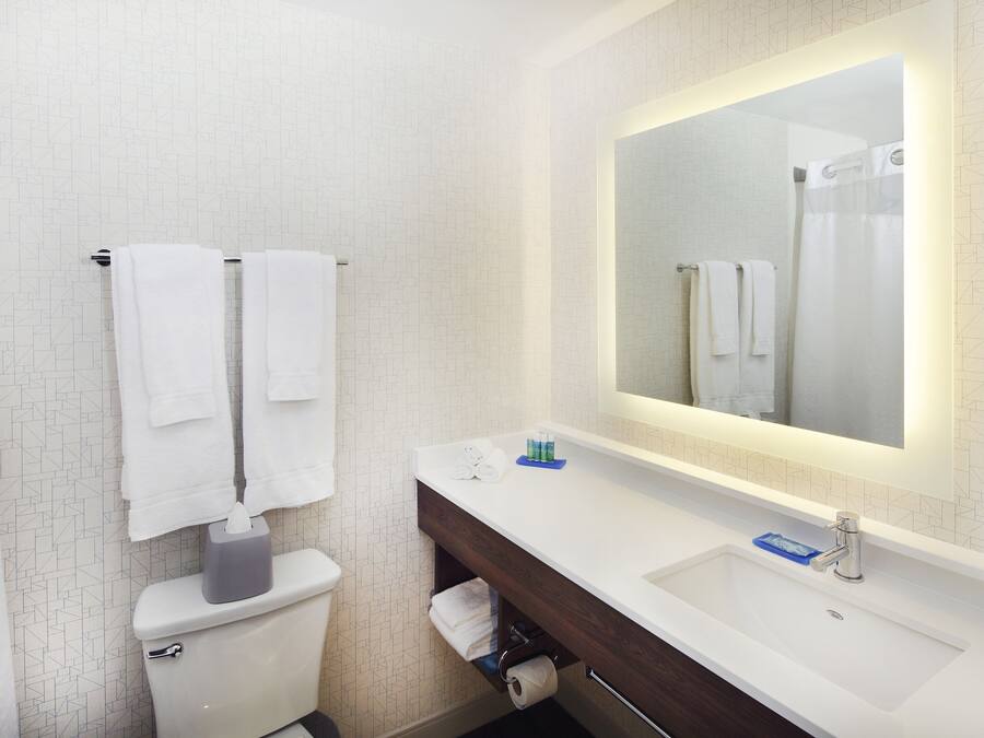 Um banheiro moderno com parede de azulejos brancos, um espelho grande, uma pia branca e um vaso sanitário.