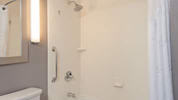 Ein Badezimmer mit Toilette, Dusche inklusive Handbrause, einer Haltestange und einem Spiegel mit Beleuchtung.
