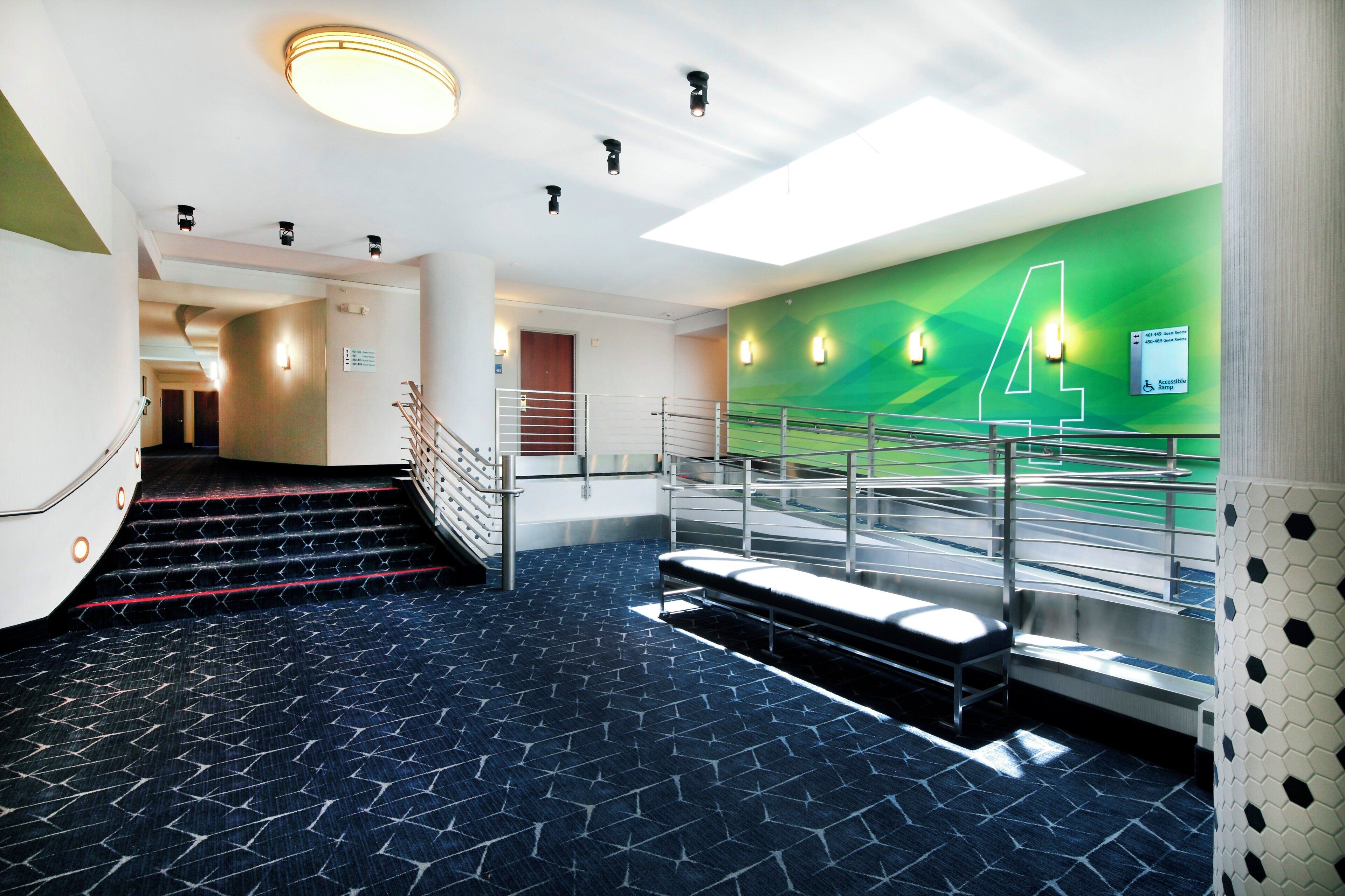 Vestíbulo moderno de hotel con una escalera, una pared verde con el número '4' y un cartel que indica habitaciones de huéspedes.