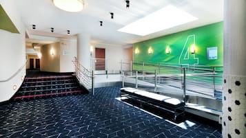 Vestíbulo moderno de hotel con una escalera, una pared verde con el número '4' y un cartel que indica habitaciones de huéspedes.