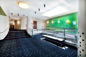 A modern hotel lobby with a staircase, a green wall with a number '4', and a sign indicating guest rooms. - Holiday Inn Express and Suites Fisherman's Wharf by IHG (San Francisco)