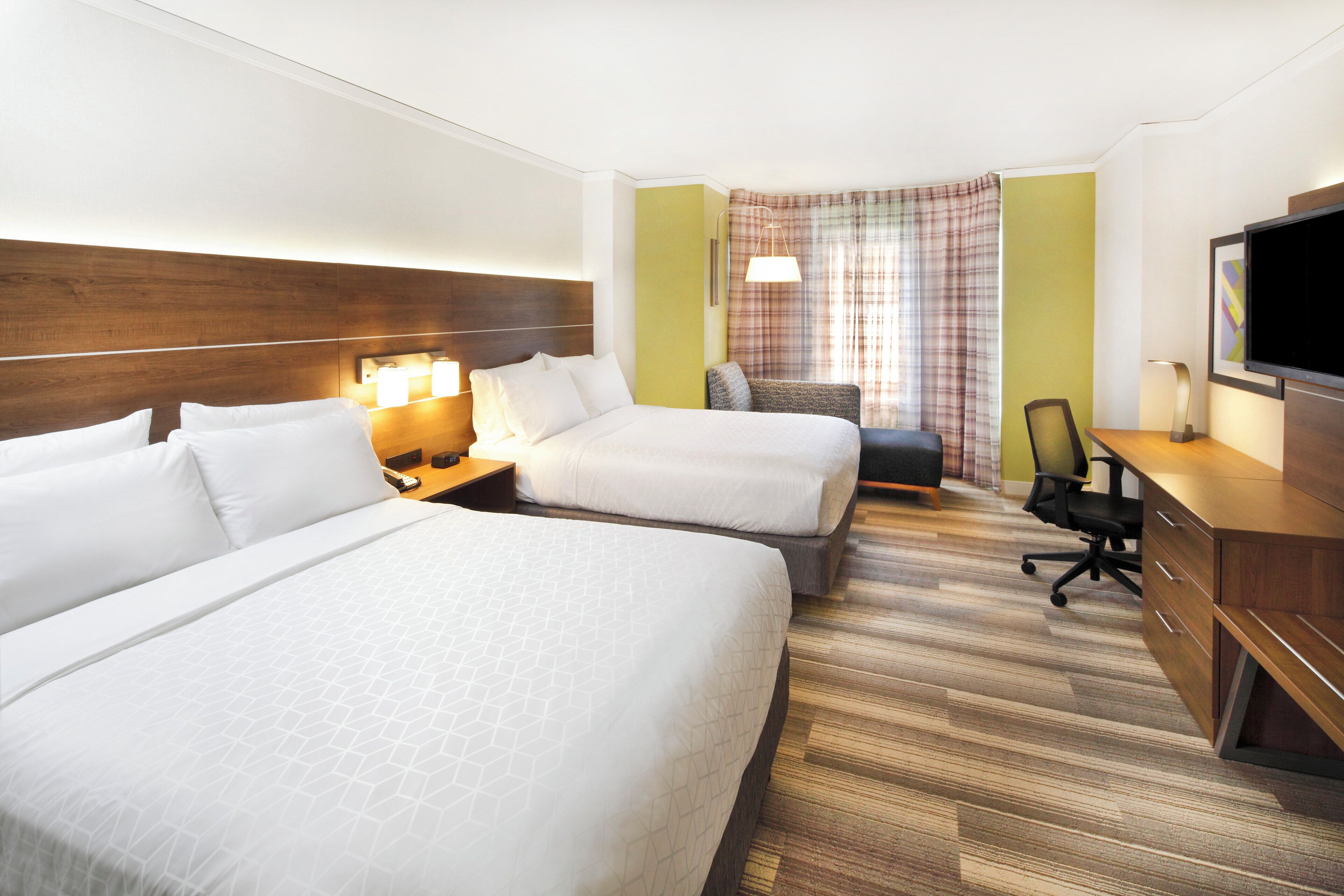 Una habitació d'hotel amb dos llits, un escriptori, una cadira i una televisió.