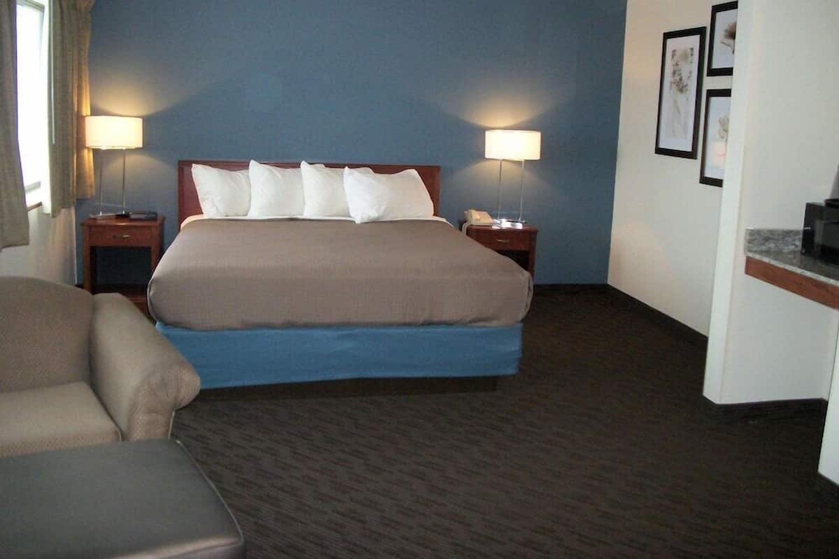 Una habitación de hotel con una cama grande, dos mesitas de noche, una silla y un escritorio con lámpara.