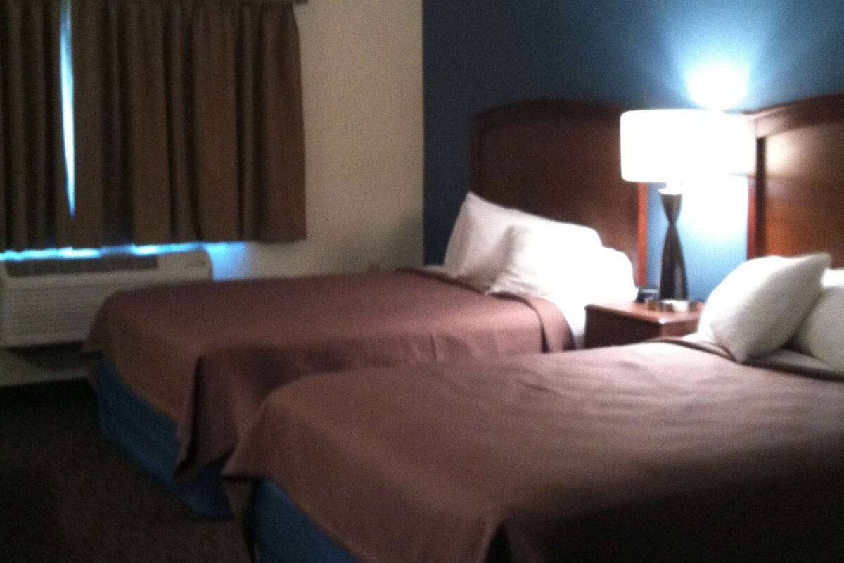 Una habitación de hotel con dos camas, una mesita de noche con lámpara, una ventana con cortinas y un radiador.