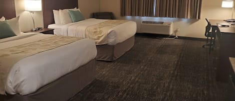Une chambre d’hôtel avec deux lits, un bureau, une chaise, un appareil de climatisation et une fenêtre avec des rideaux.