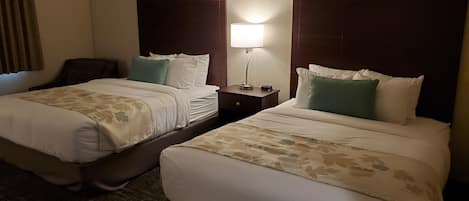 A hotel room with two beds, each with a headboard, a bedside table, and a lamp.