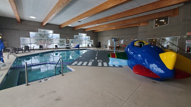 Una piscina interior con vigas de madera, amplias ventanas de vidrio y una decoración de un avión colorido.
