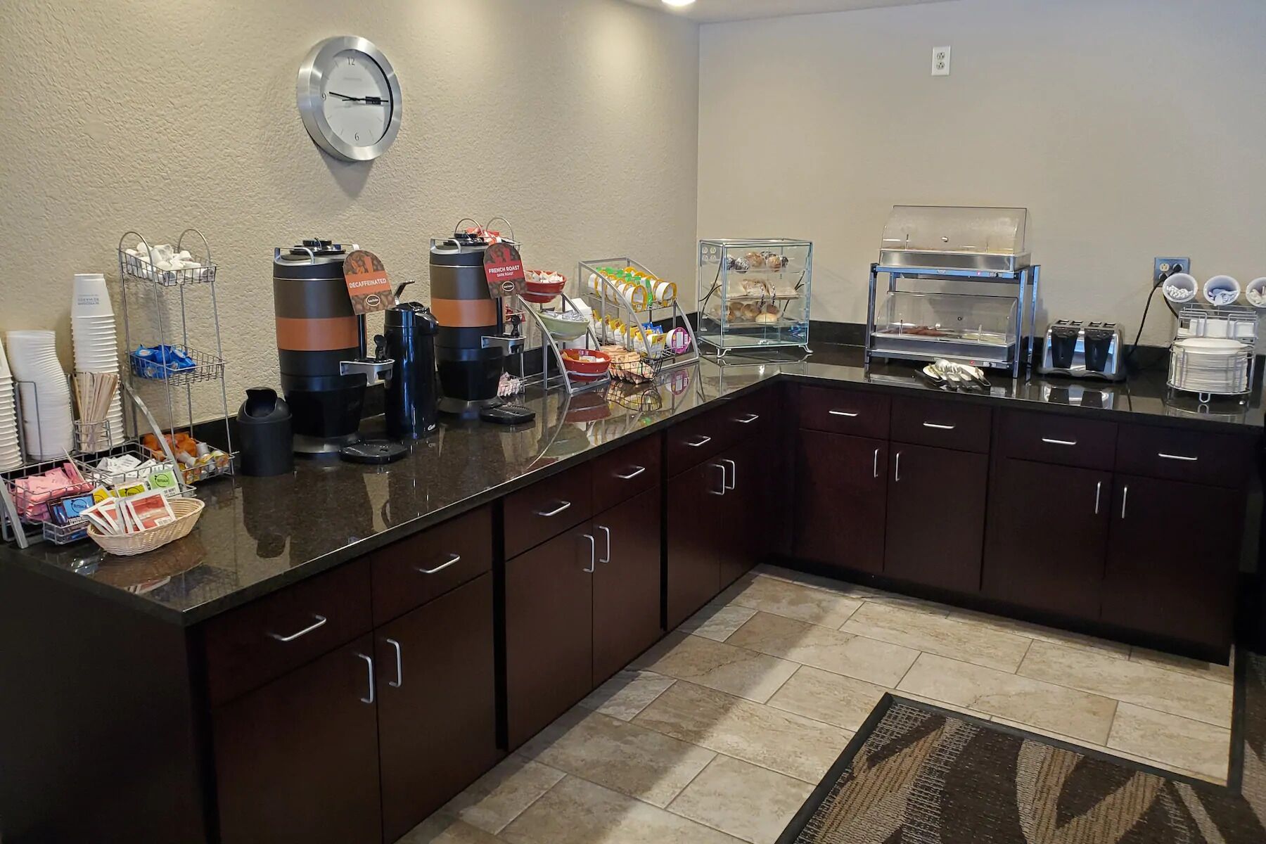 A hotel kitchen with a coffee station, a clock, and various food items displayed.