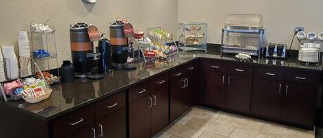 A hotel kitchen with a coffee station, a clock, and various food items displayed.