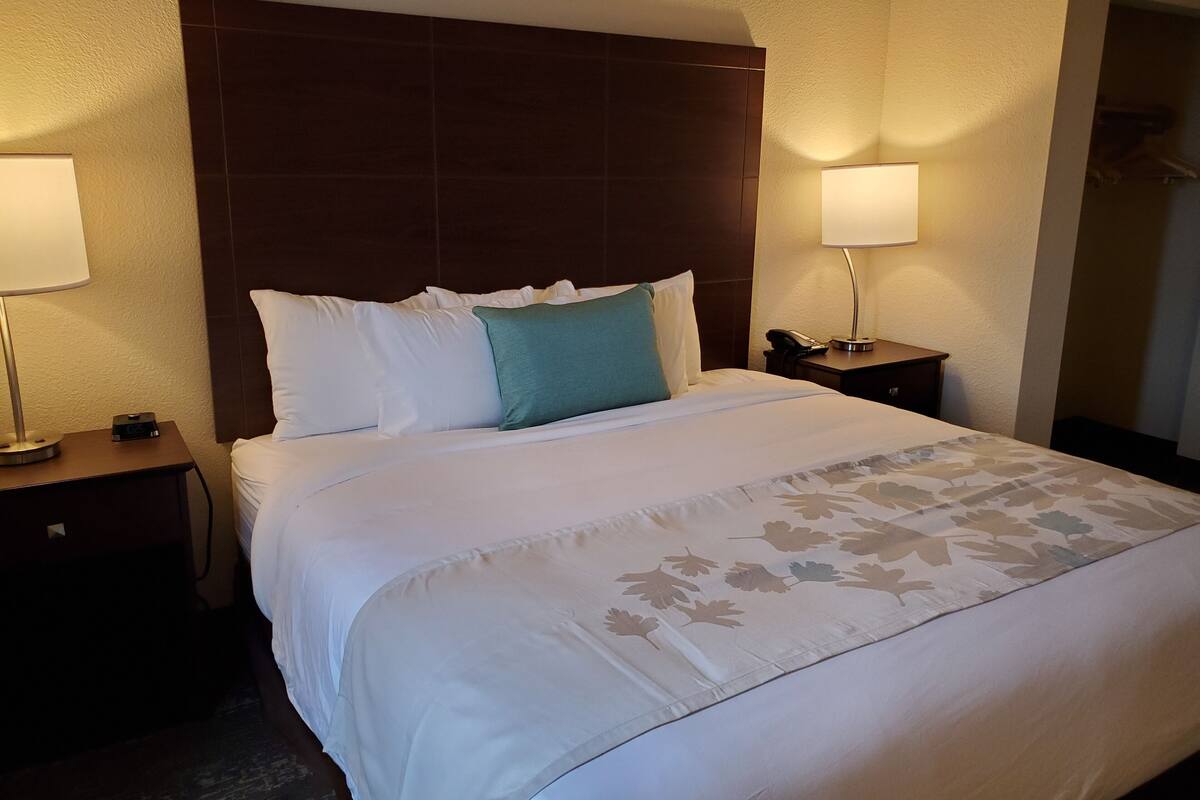 A hotel room with a large bed, two bedside tables, a nightstand, and a lamp on each side.