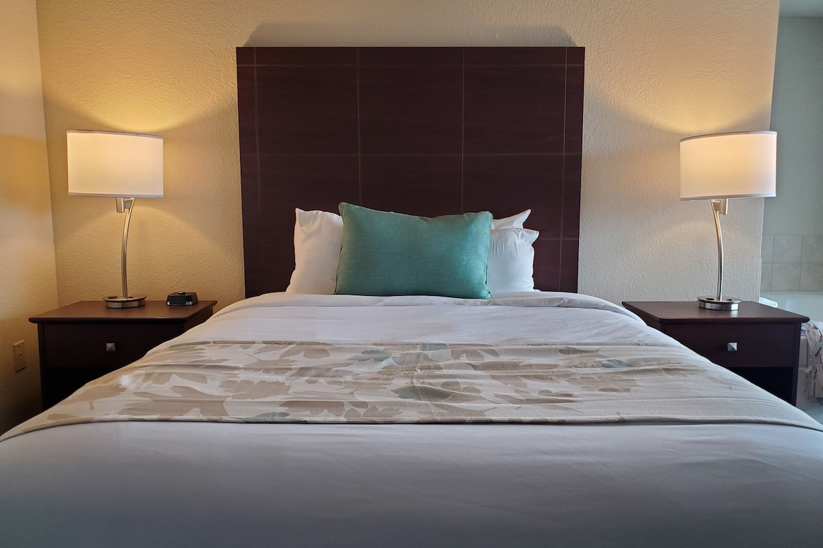 A hotel room with a large bed, two bedside tables, and two lamps.