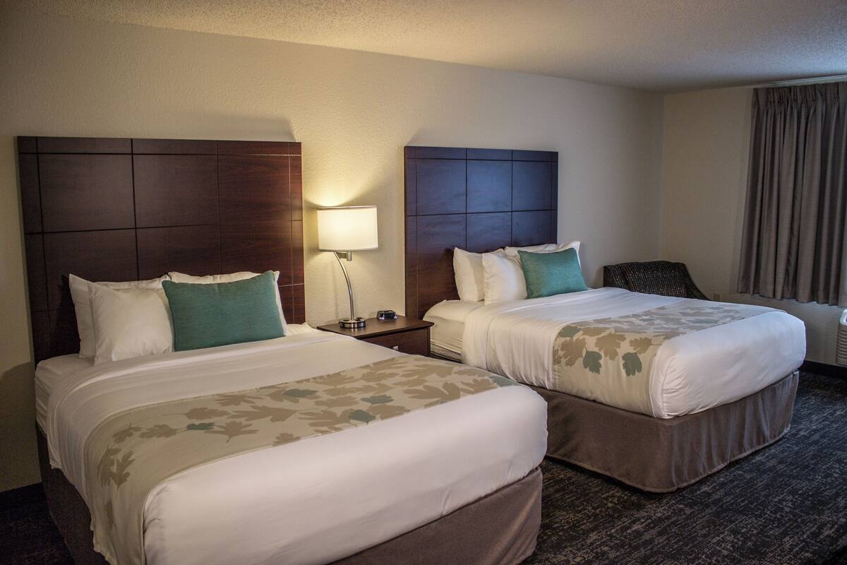 A hotel room with two beds, a nightstand, a lamp, and a chair.