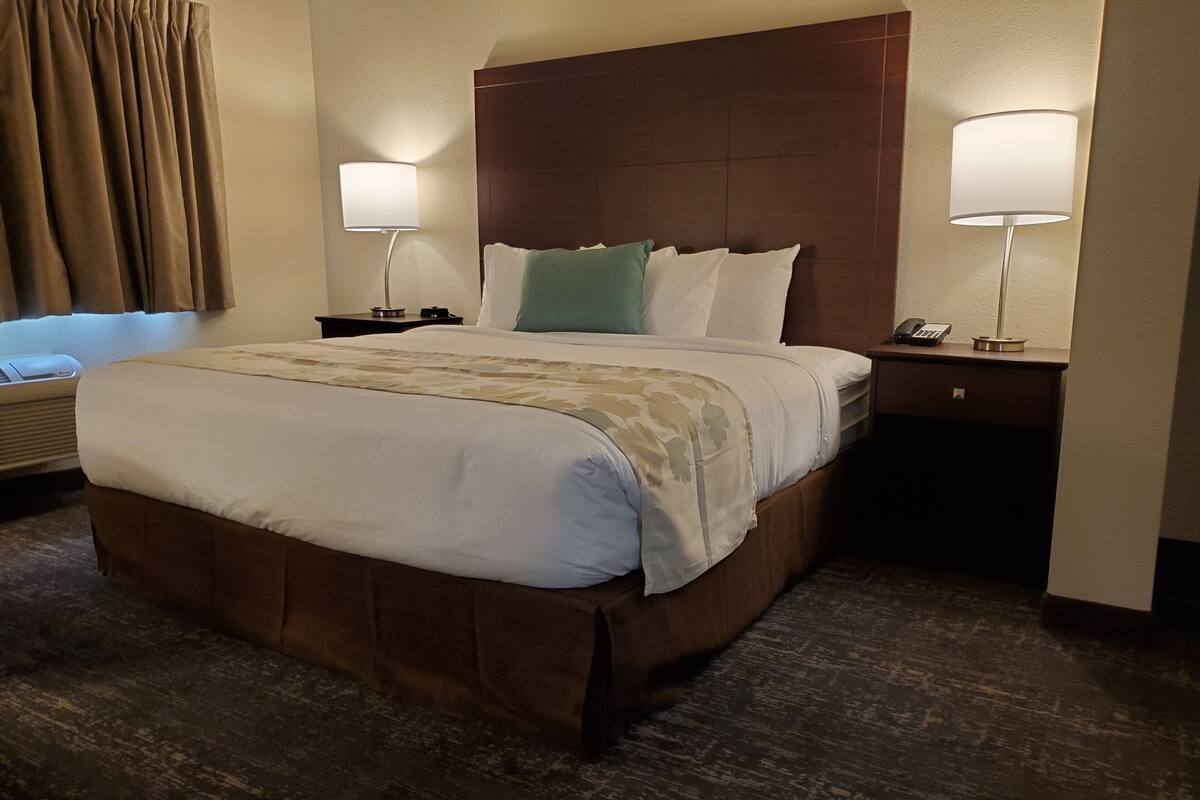 A hotel room with a large bed, two bedside tables with lamps, a headboard, and a window with curtains.