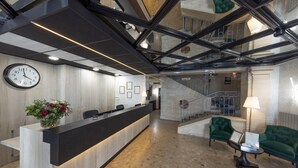 Un área de recepción moderna con un mostrador, un reloj, un sofá verde y una escalera que sube a un nivel superior.