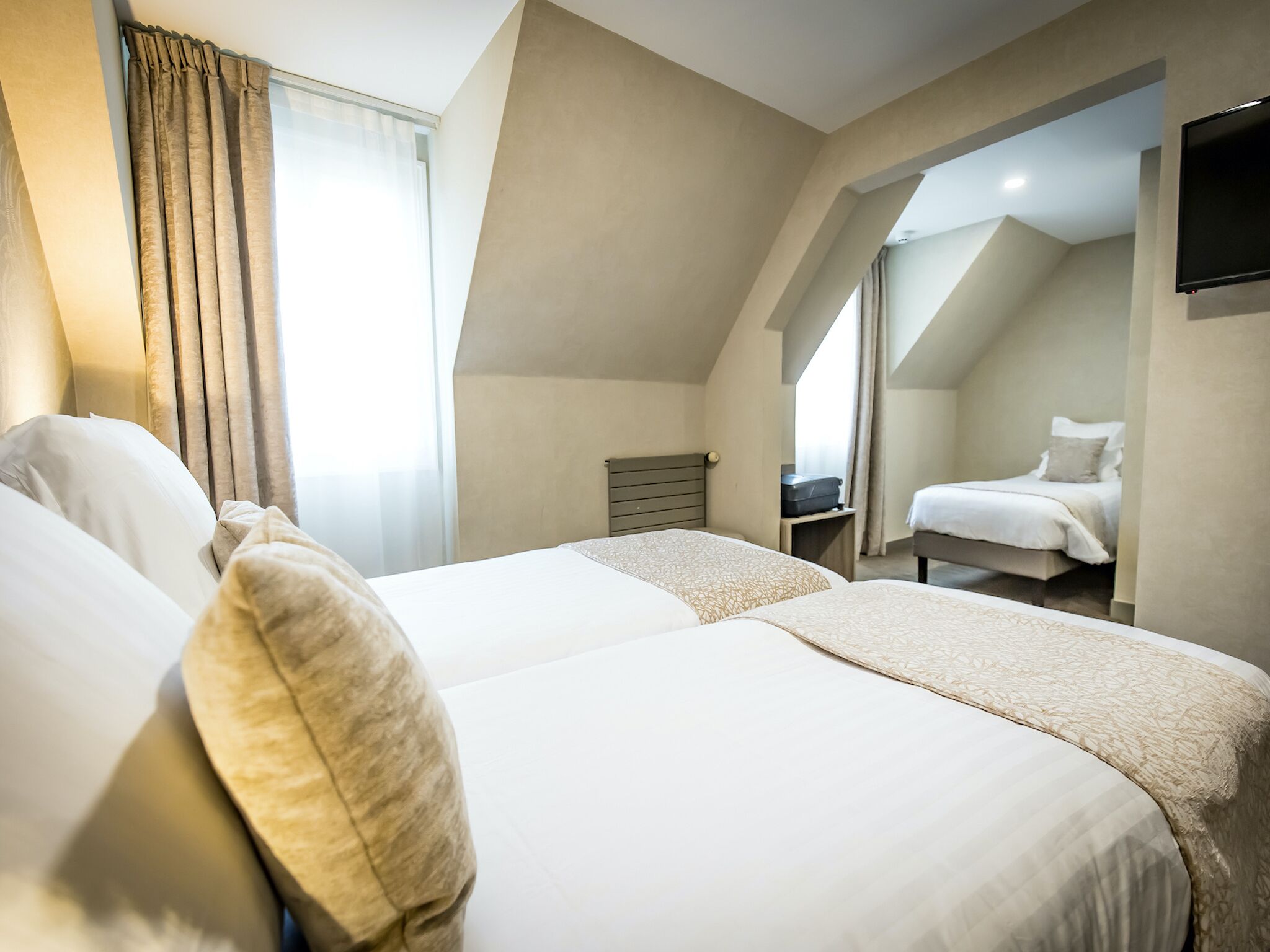 Habitación de hotel con dos camas, televisión y vista a otra habitación.