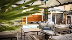Un espacio de estar al aire libre cubierto, con piscina, sillas de descanso y una mesa.