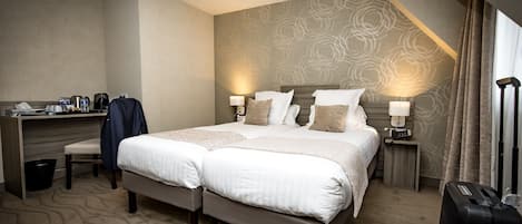 A hotel room with a large bed, a desk with a chair, a suitcase, and a wall-mounted lamp.