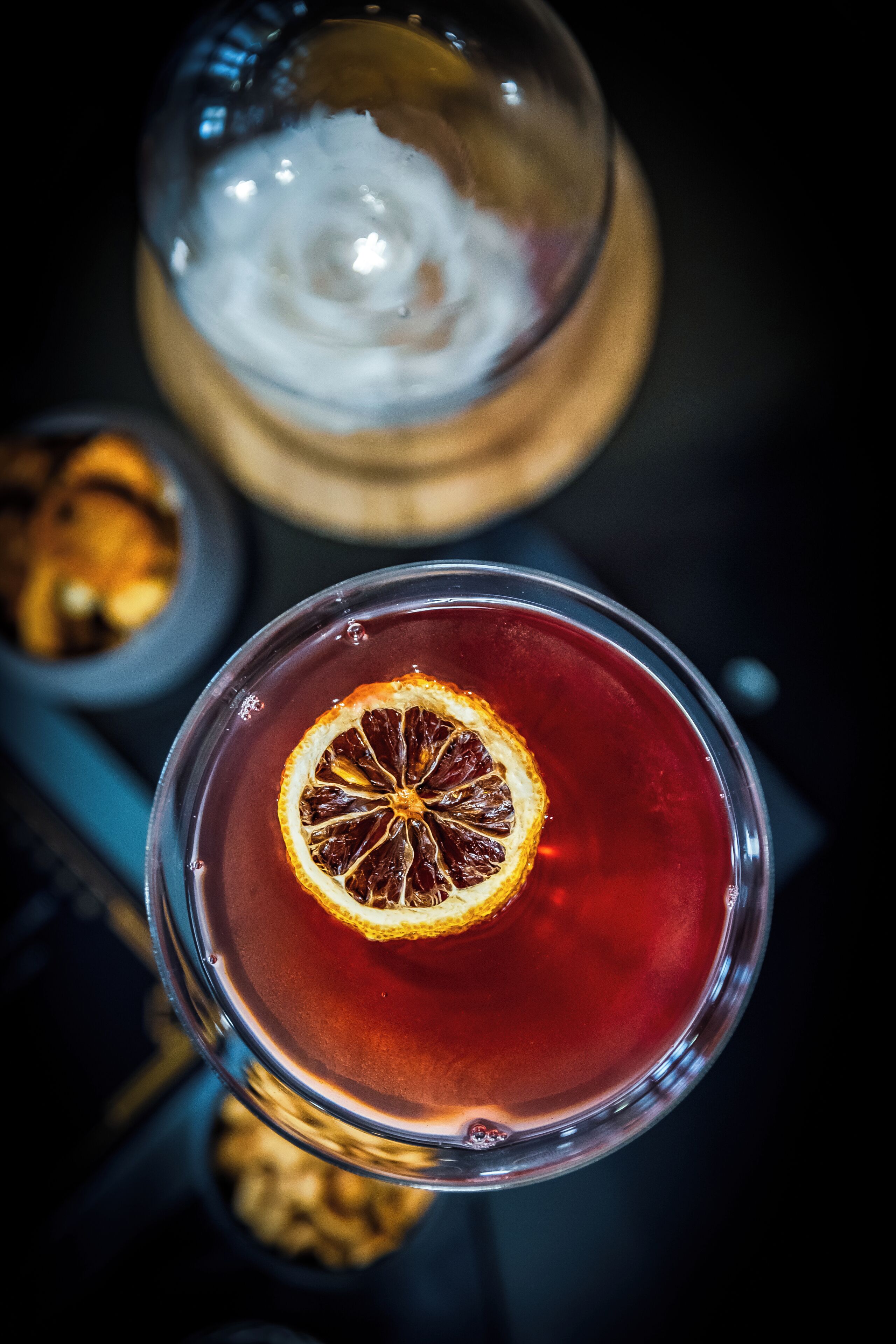Un verre d’une boisson rouge, garni d’une tranche d’orange séchée et de glaçons, et un verre d’une boisson blanche surmontée d’une mousse.
