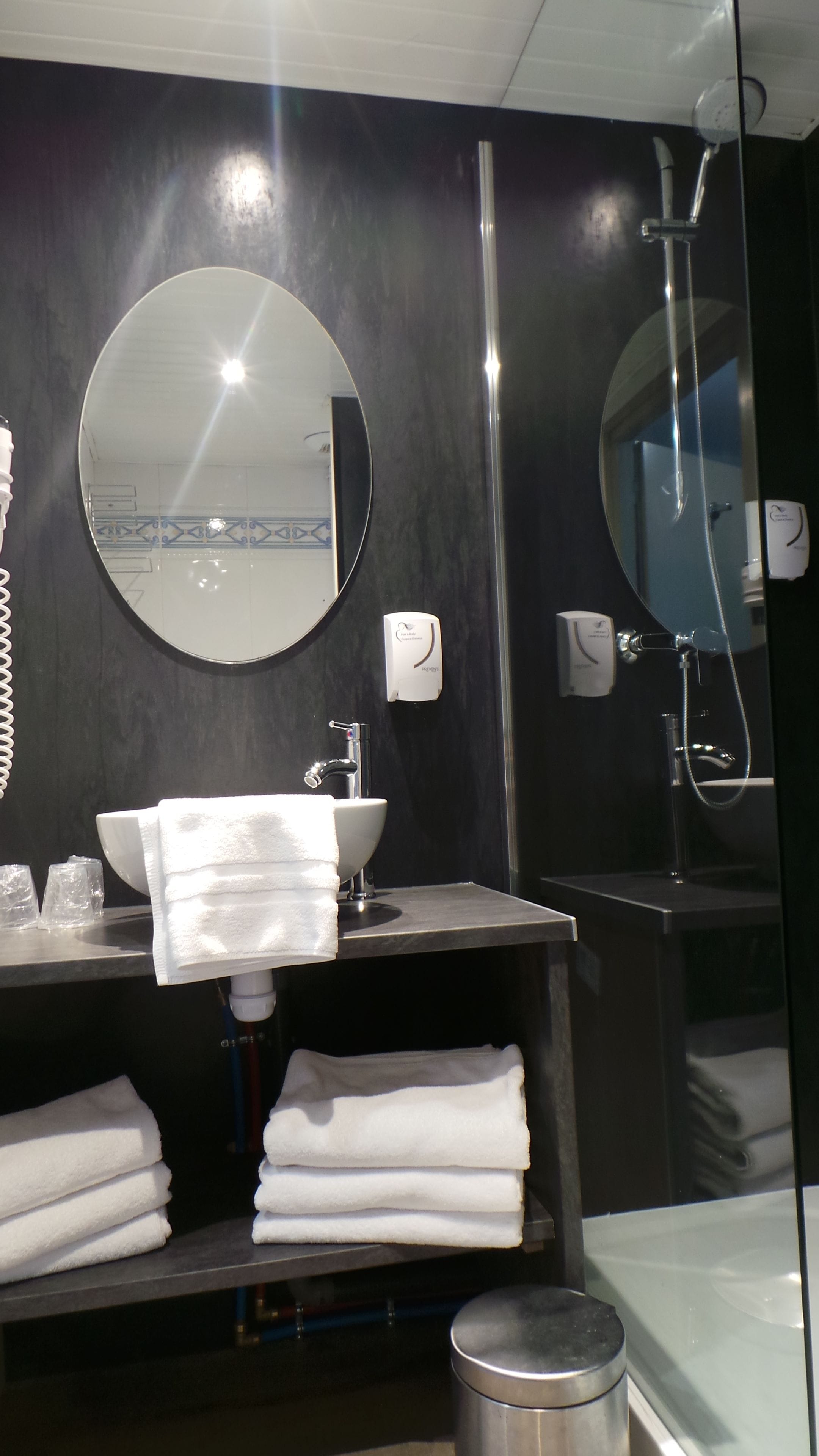 A bathroom with a round mirror, a sink, a towel rack, and a shower.